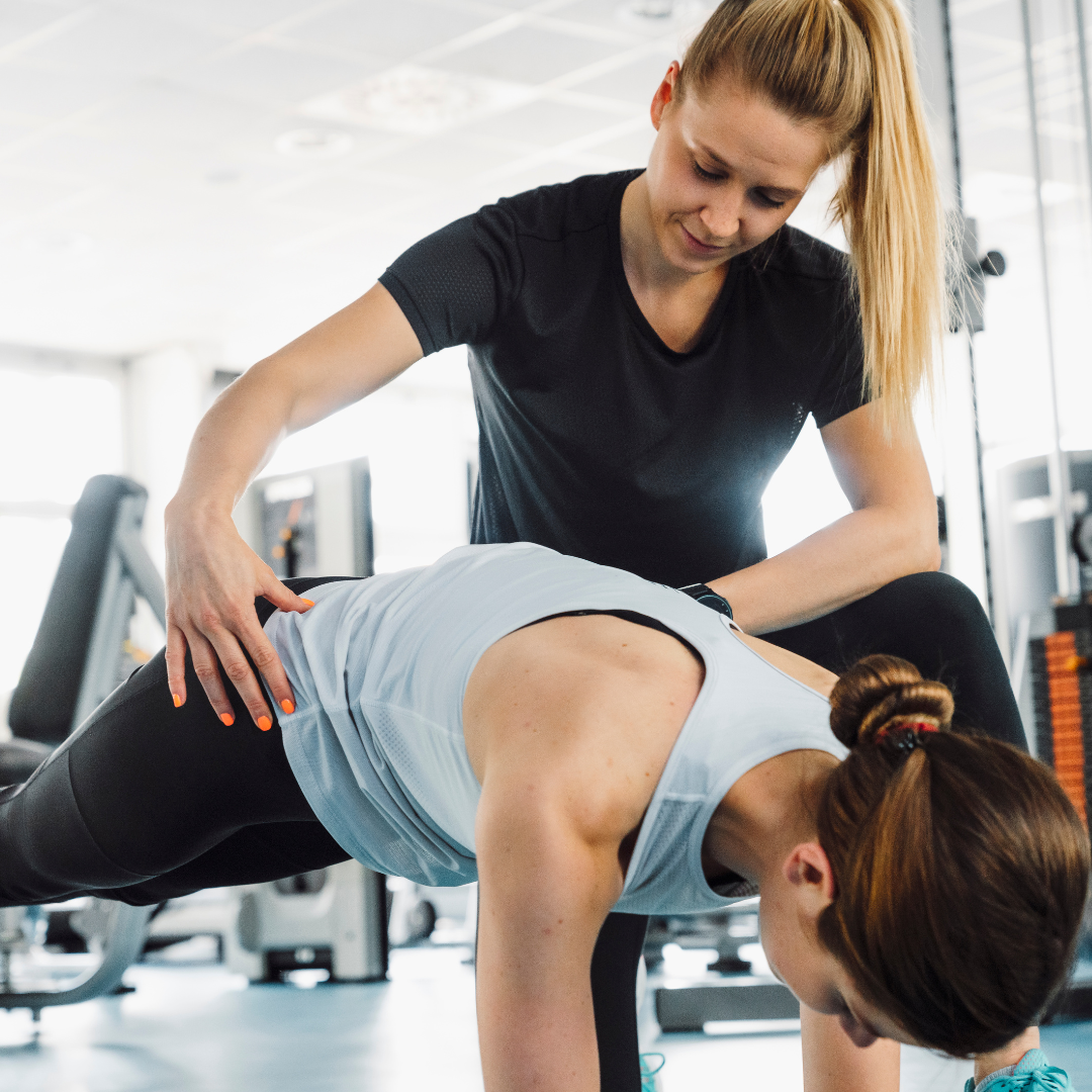 Fitness trainer manually correcting a trainees movement of her back