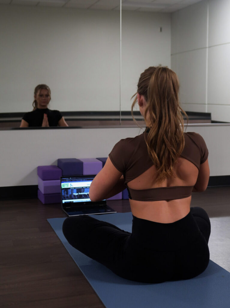 Woman with legs crossed at a studio in front of a laptop for a yoga training month workshop