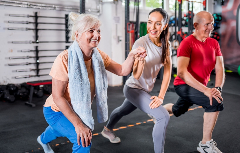 Personal trainer exercising and holding hand of senior woman